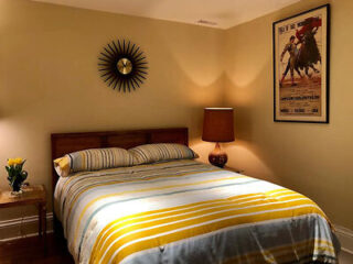 A warmly lit bedroom with a striped bedspread, vintage-style lamp, and a classic movie poster on the wall