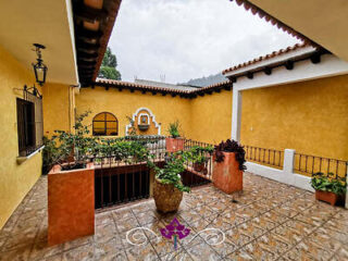 A charming courtyard with yellow walls, potted plants, and a tiled floor, featuring a small fountain in the background.