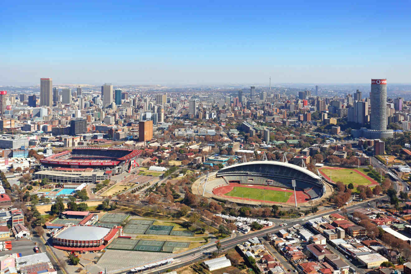 Aerial view of a cityscape featuring multiple sports stadiums, surrounding buildings, and a clear sky.