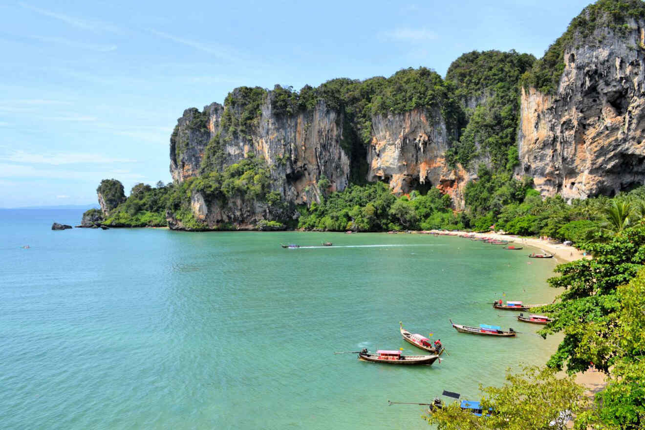 A picturesque beach with towering cliffs, turquoise water, and traditional boats.