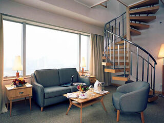A hotel suite with a spiral staircase, a seating area with a sofa, chairs, and a coffee table.