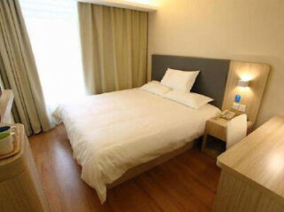 A minimalist hotel room with a double bed, wooden furniture, and soft lighting.
