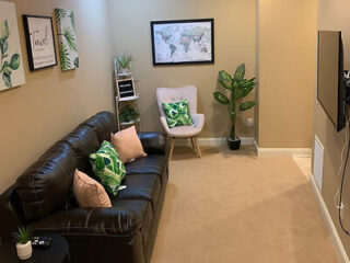 A cozy living room with a black leather sofa, green-themed pillows, and a wall-mounted TV.