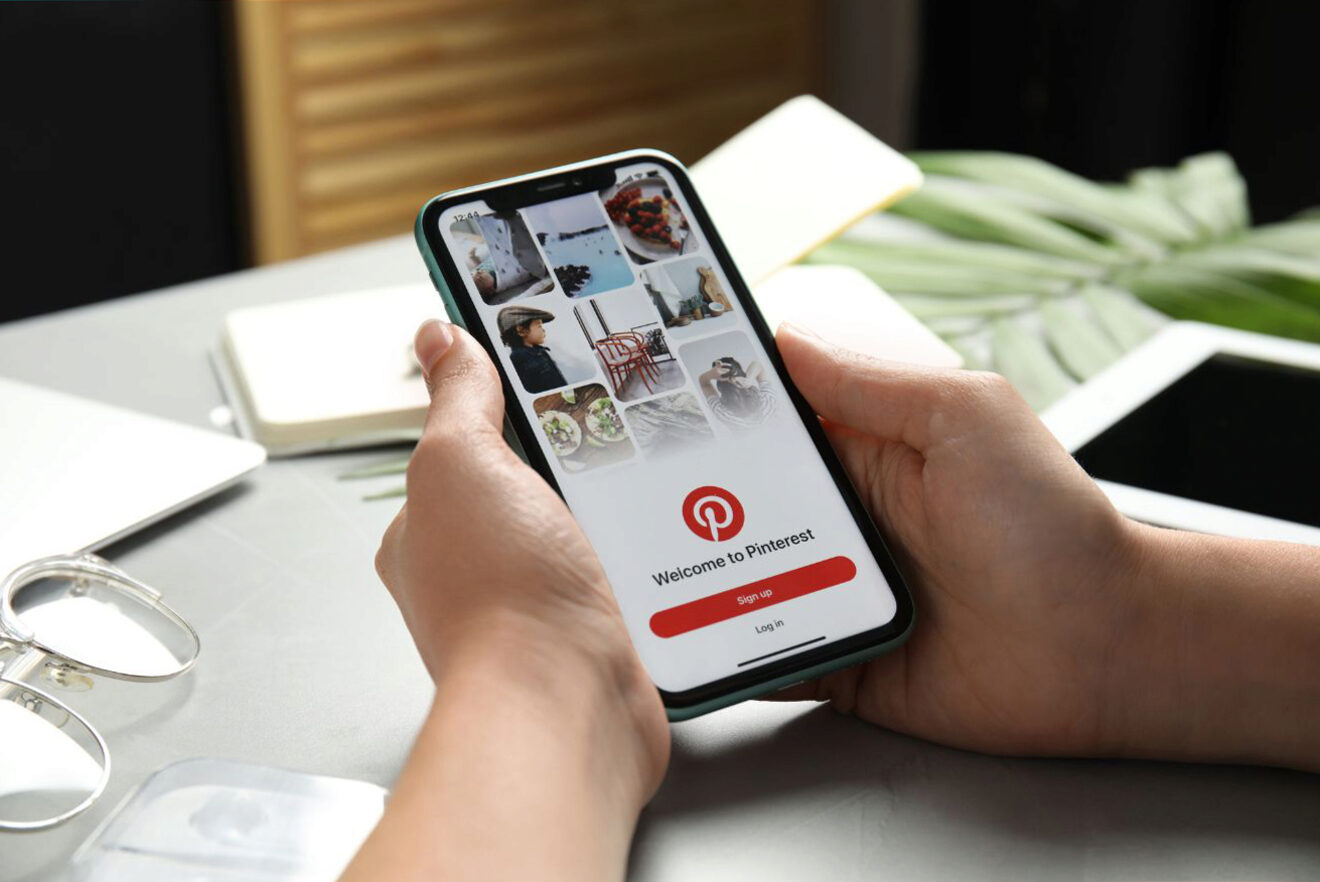 A person holding a smartphone displaying the Pinterest welcome screen with 