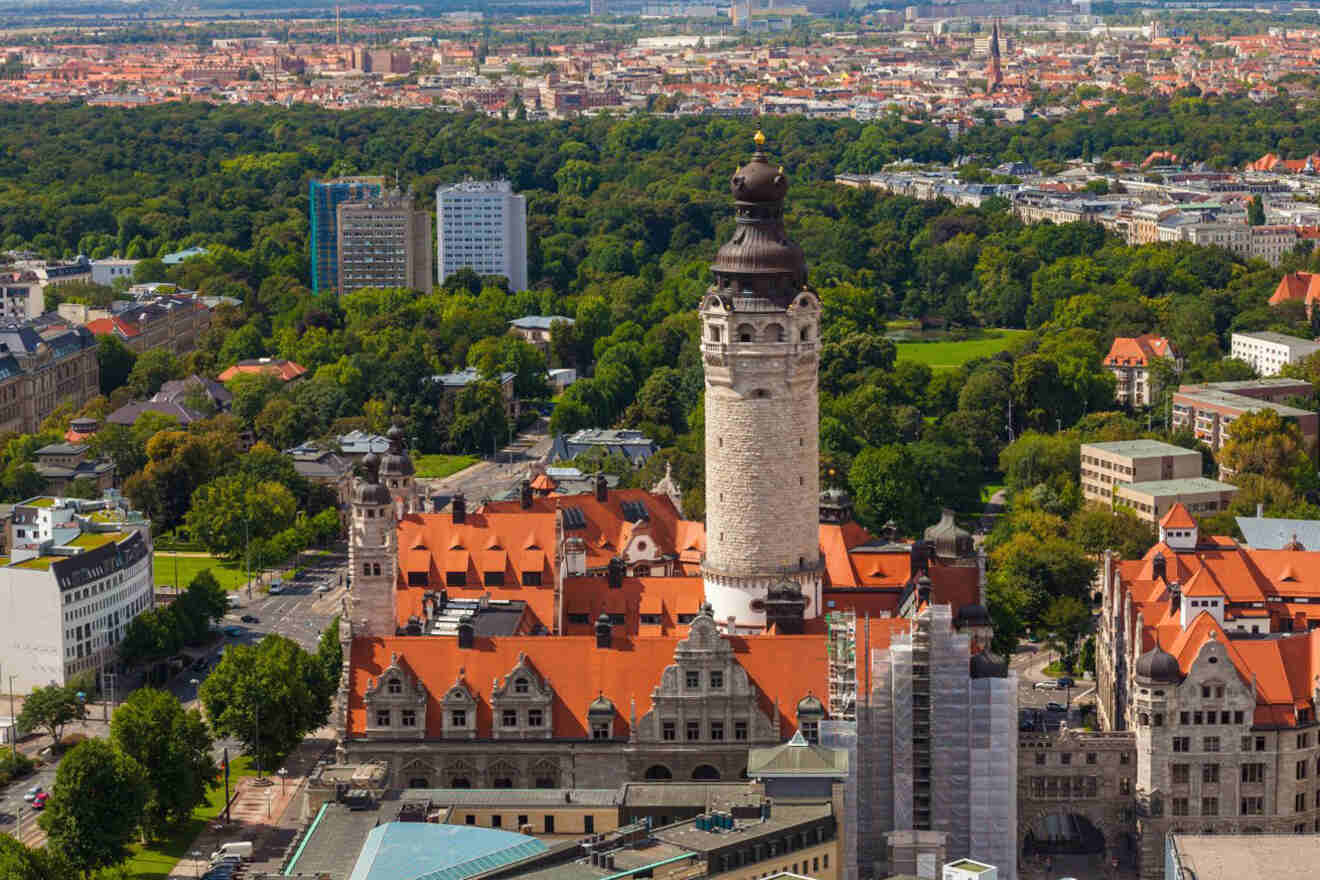 Aerial view of a cityscape featuring a historic tall tower surrounded by lush green trees and buildings with red roofing.