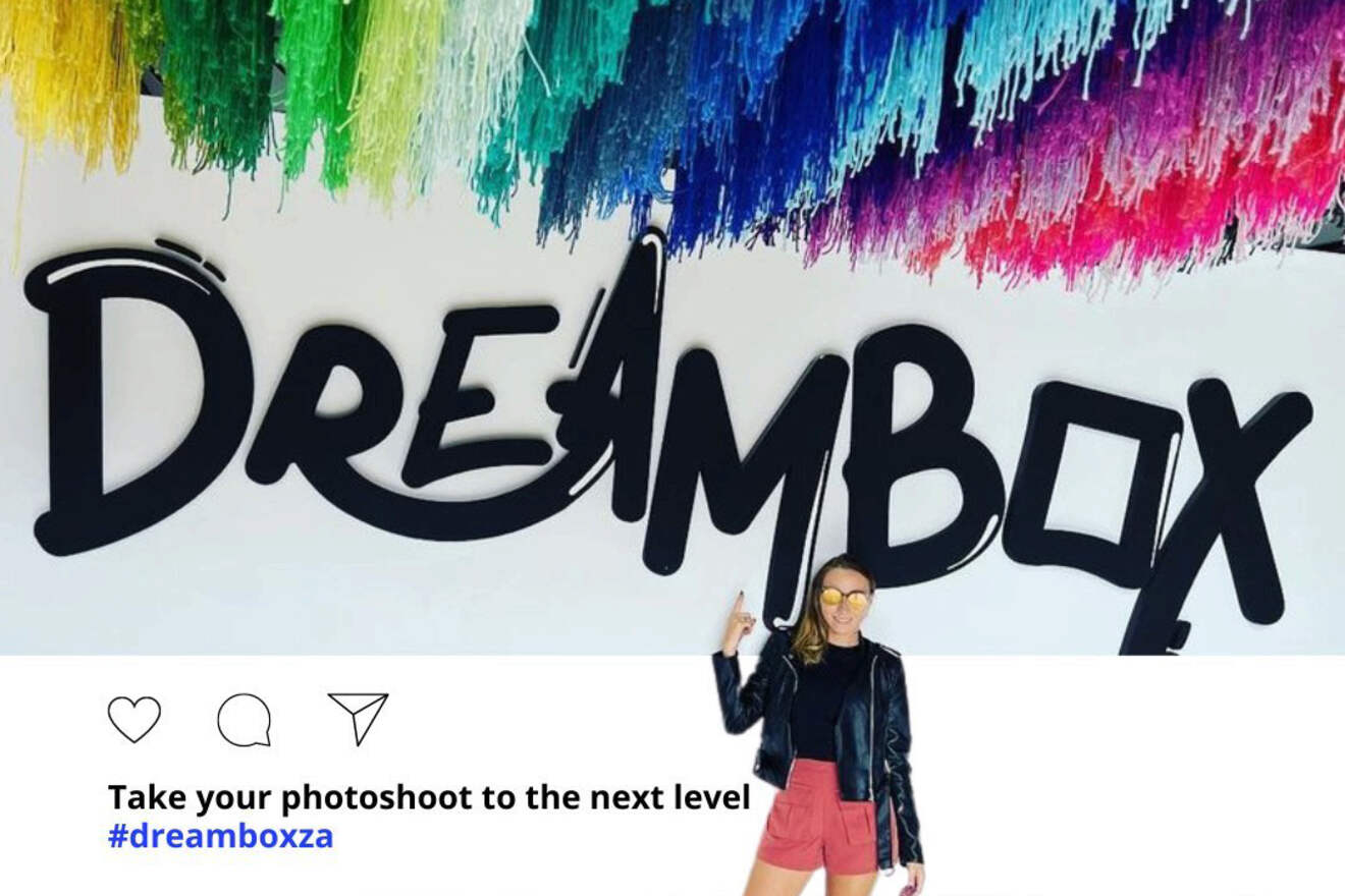 A person in red shorts and a black jacket poses in front of a wall with the word "DREAMBOX" and colorful fringed decorations. The caption reads: "Take your photoshoot to the next level #dreamboxza".
