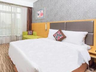 A bright hotel room with a large bed, a colorful chair, and a decorative pillow.