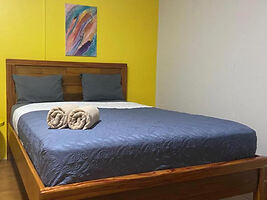 A bedroom with a yellow accent wall, wooden bed frame, and blue bedding.