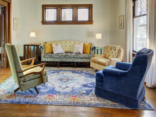 A vintage-styled living room with colorful armchairs, a patterned rug, and a sofa.