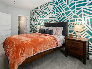 A bedroom with a bold, geometric accent wall, an orange blanket, and two bedside lamps.