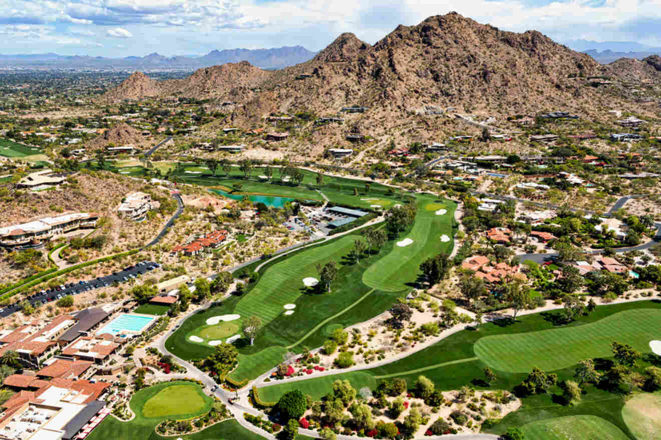 An aerial view of a lush golf course nestled among desert mountains and residential areas.