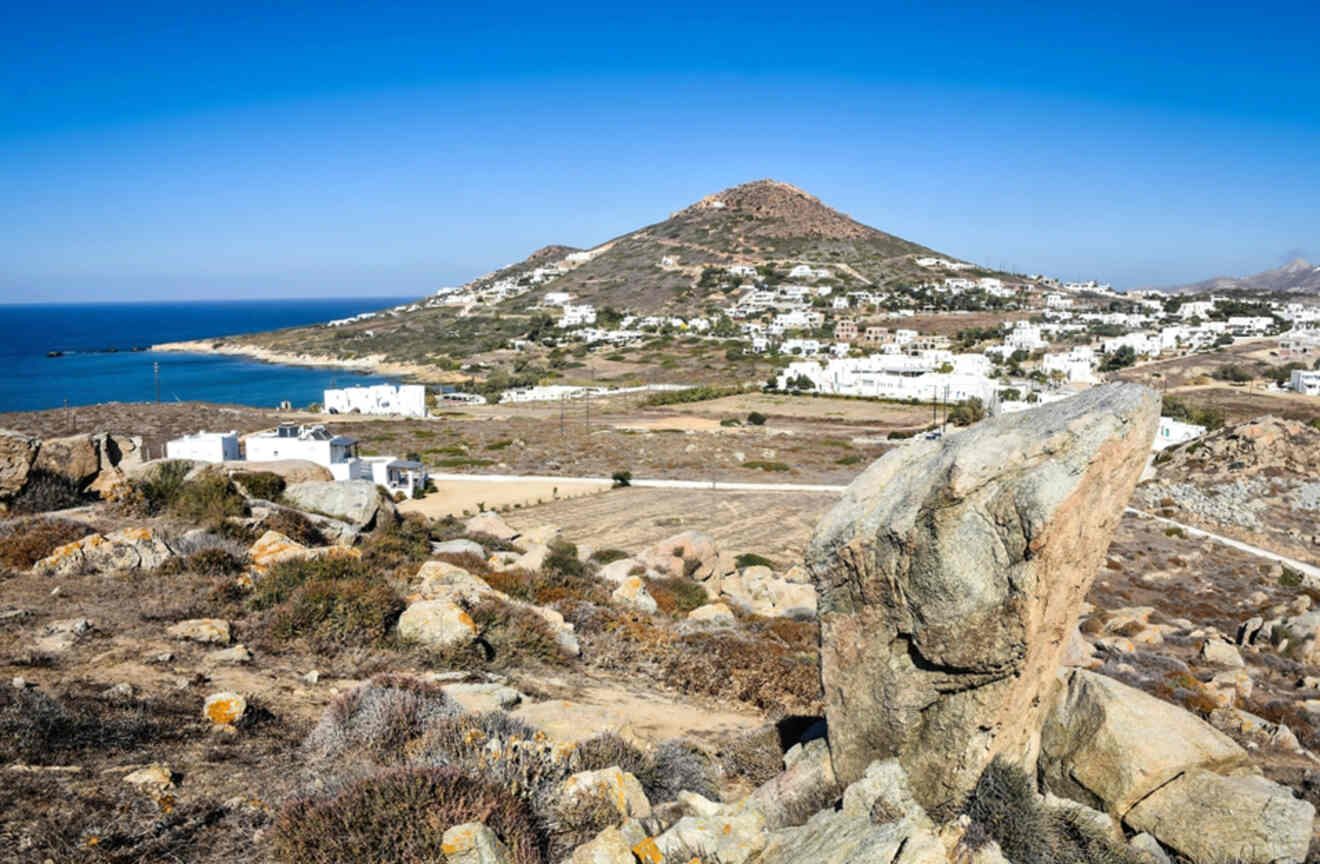 A panoramic view of a coastal town with white buildings, a mountainous backdrop, and the sea under a clear blue sky.