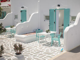 Outdoor seating area with white walls, light blue shutters, and turquoise furniture, giving a cozy and inviting feel.
