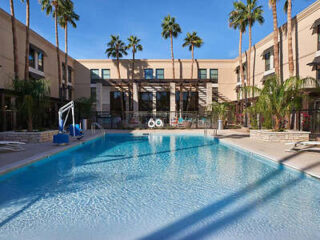 An outdoor hotel pool surrounded by palm trees and a sunlit hotel building