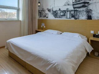 A simple hotel room with a large bed, wooden headboard, and a mural on the wall behind the bed.