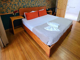 A cozy bedroom with a large bed, colorful pillows, and wooden flooring.