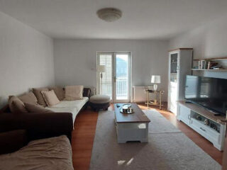 A spacious living room with a large beige sofa, coffee table, and TV, illuminated by natural light from a balcony door