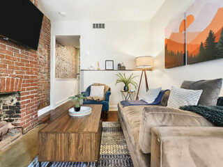 A charming living room with exposed brick, a comfy sofa, and vibrant wall art.