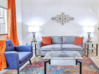A cozy living room with a gray sofa, a blue armchair, and orange accents on the pillows and curtains