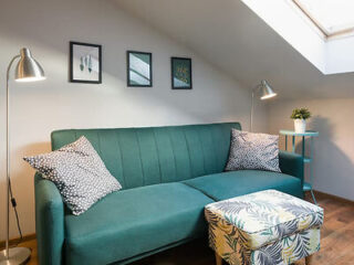 A small living area with a teal sofa, patterned cushions, a floral ottoman, and wall art, lit by two modern floor lamps.