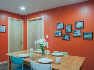 A dining area with a wooden table set for four against a bold orange wall decorated with black-and-white photos.