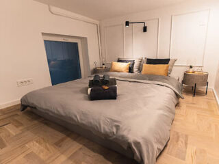 A cozy bedroom with a low double bed, gray bedding, and ambient lighting, featuring a small window.