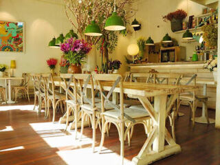 A cozy restaurant with wooden tables and chairs, decorated with vibrant flowers and green pendant lights.