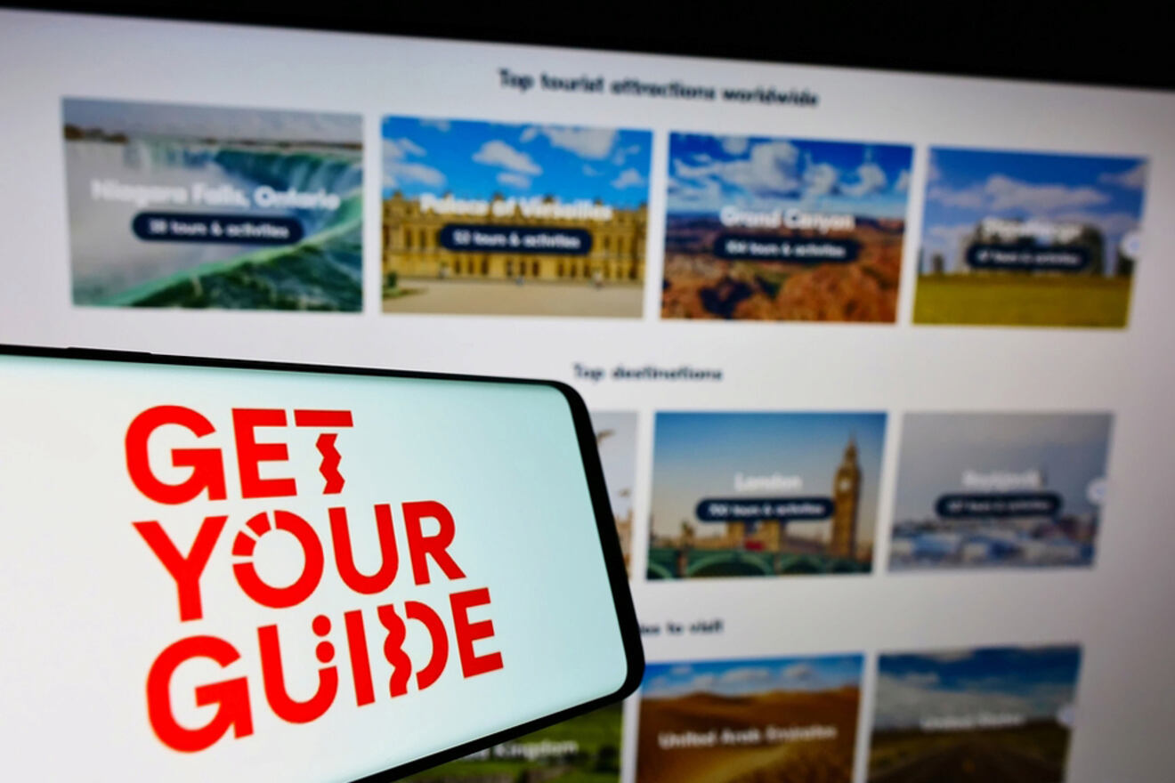 A phone displaying the "Get Your Guide" logo is held in front of a screen showing various tourist attractions and destinations worldwide, including Niagara Falls, Versailles, and the Grand Canyon.