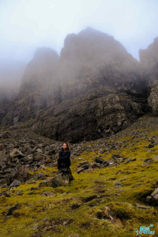 Author of the post sits on a rock in front of a misty, rugged mountain landscape with green moss covering the ground.