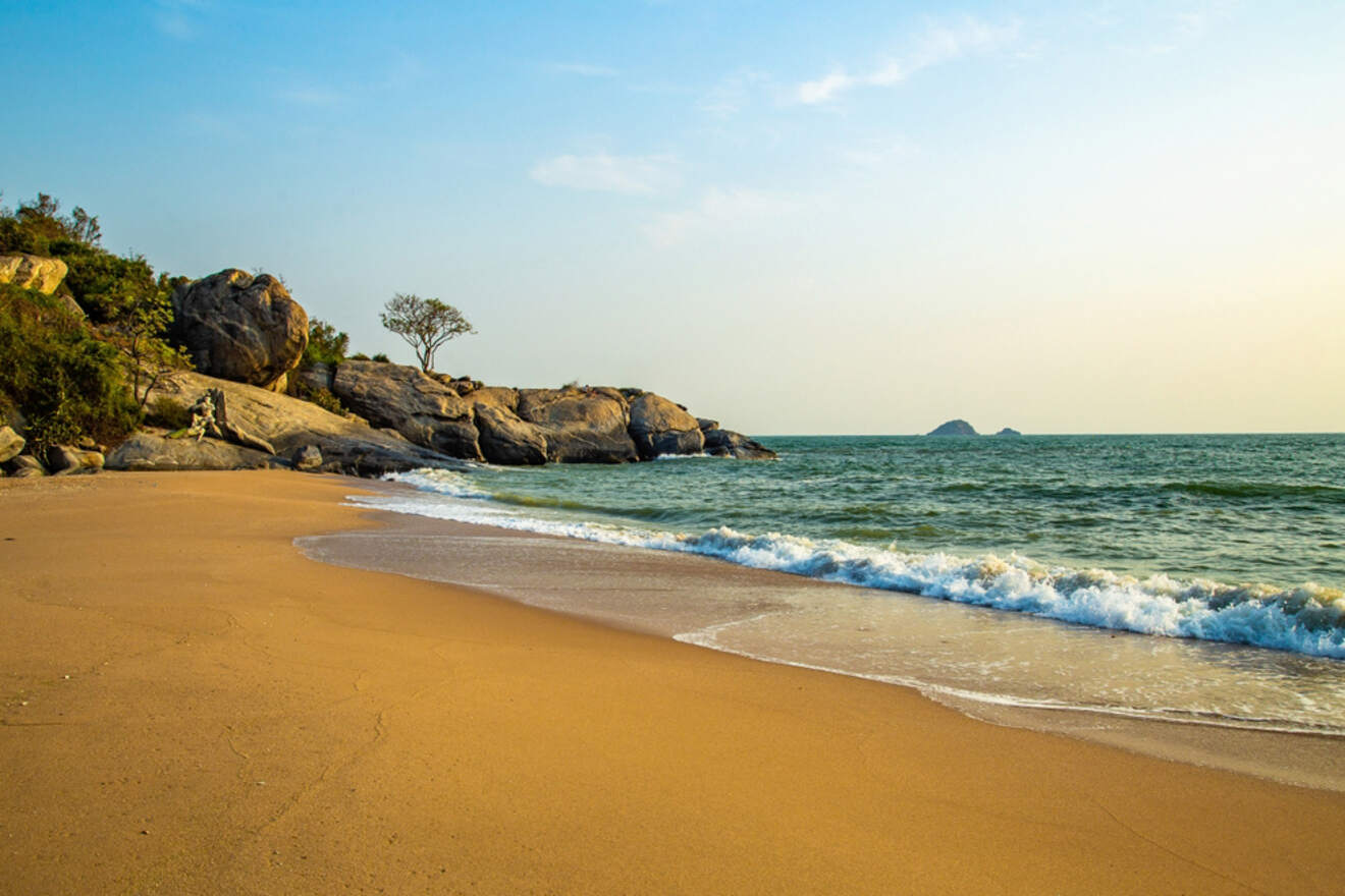 A tranquil sandy beach with gentle waves and scattered boulders.