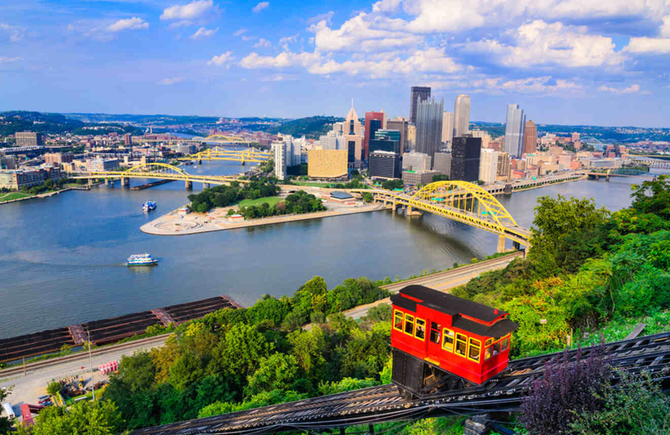 An iconic red funicular car ascending a hillside with a panoramic view of Pittsburgh's rivers and cityscape.