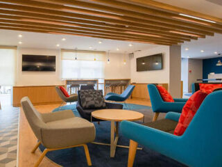 A modern lounge area with colorful chairs, wooden ceiling accents, and multiple TVs on the walls