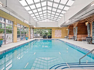 An indoor pool with a glass roof, surrounded by seating and lush greenery.