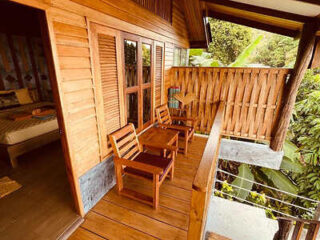 A cozy wooden balcony with chairs, offering a serene view of the tropical foliage.