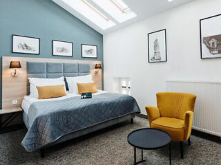 A modern bedroom with a large bed, gray and mustard-yellow accents, and skylights providing natural light.