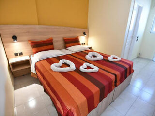 A twin bedroom with red and orange bedding, featuring towel decorations shaped like hearts on the beds.