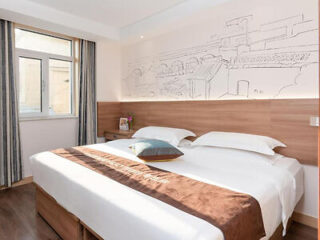 A bright hotel room with a large bed, wooden headboard, and a mural sketch on the wall.