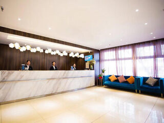 A sleek hotel reception area with a marble desk, friendly staff, and a blue sofa with colorful pillows.