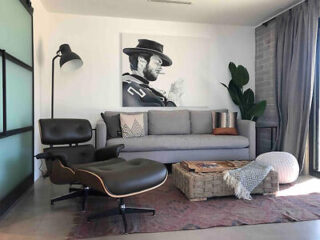 A stylish living room with a gray sofa, a black lounge chair, and a large black-and-white artwork of a man on the wall
