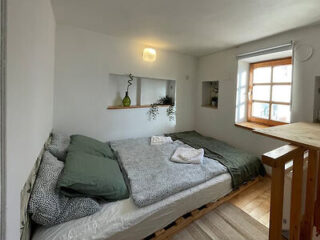 A small bedroom with a double bed, green bedding, and a window letting in natural light.