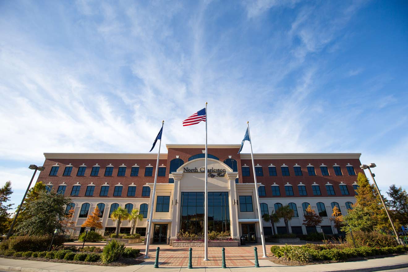 Exterior view of the North Charleston City Hall building with an American flag and clear blue sky above.
