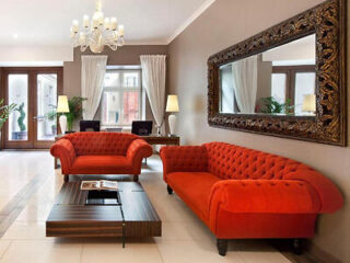 A luxurious hotel lobby with red tufted sofas, a large mirror, and elegant lighting fixtures.