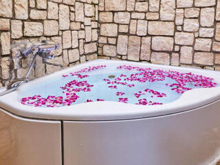 A luxurious bathtub filled with water and flower petals, set against a rustic stone wall.