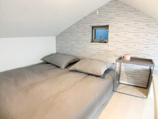 A minimalist bedroom with a low double bed under a sloped ceiling, featuring a small window