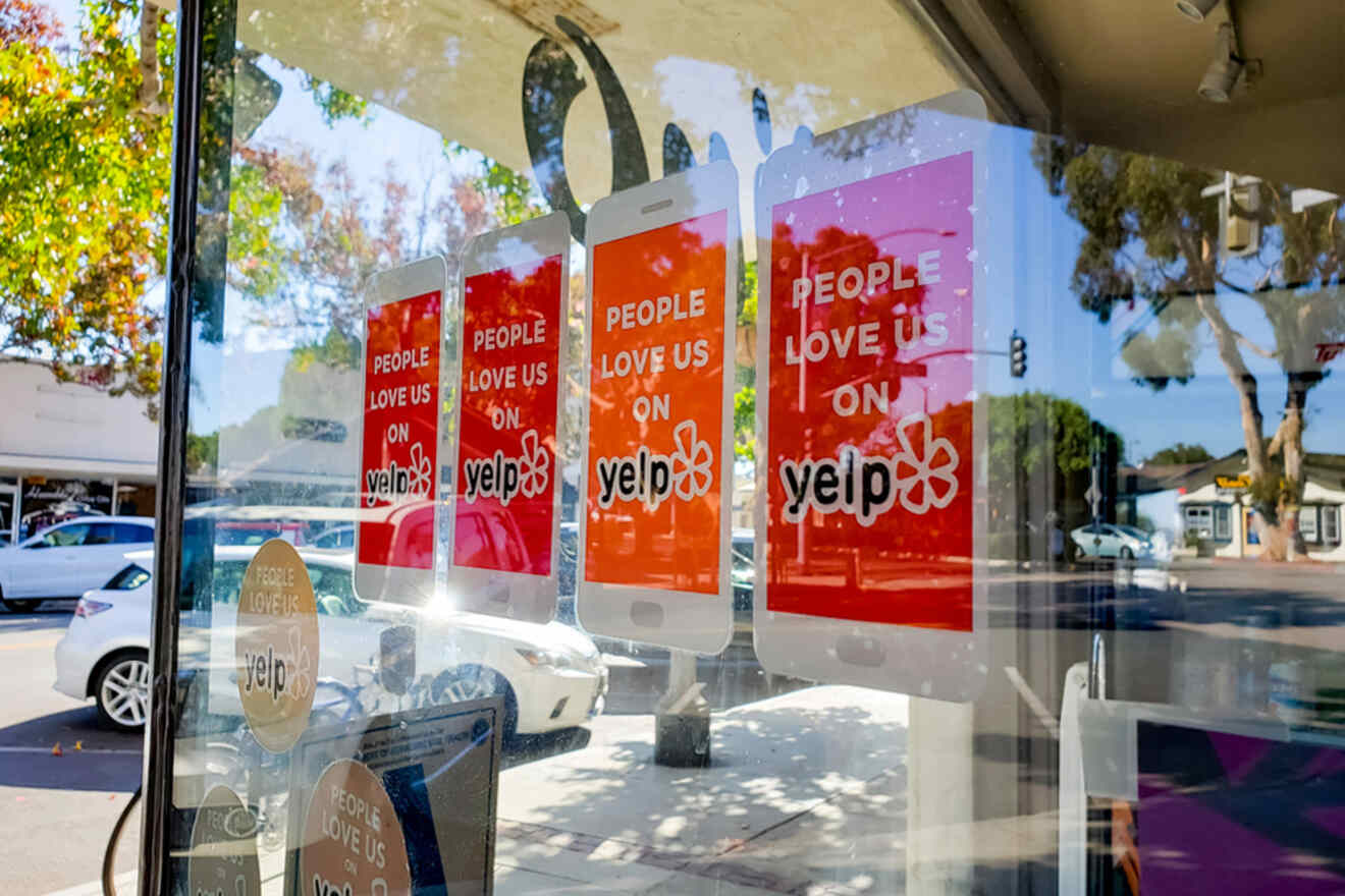 Glass storefront with three red "People love us on Yelp" signs displayed, reflecting trees from outside.