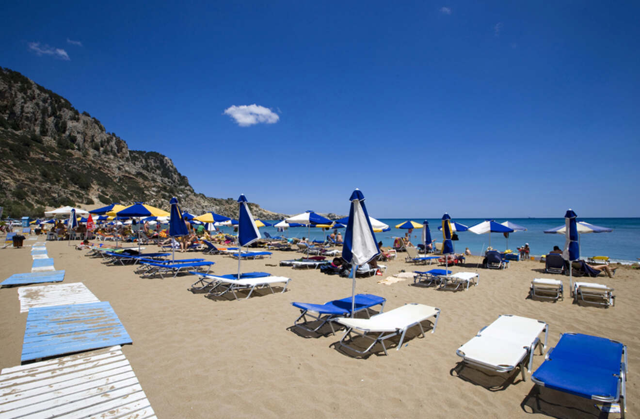 A sandy beach filled with sun loungers and umbrellas, with people enjoying the sunny day and the blue sea.