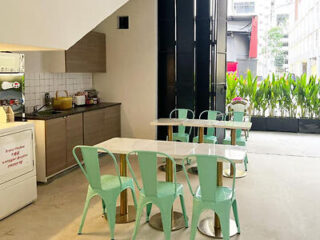 A small dining area with pastel green chairs, white tables, and an open view of greenery outside.