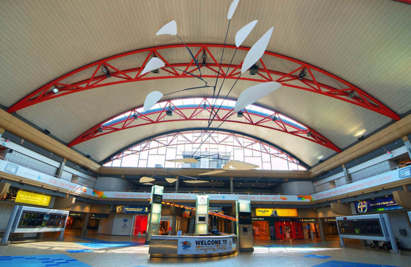 The interior of an airport terminal featuring a high arched ceiling with red beams and a welcome sign