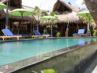 A serene pool area with green umbrellas and blue lounge chairs in front of thatched-roof bungalows