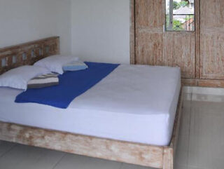 A simple bedroom with a rustic wooden bed, white and blue bedding, and a wooden wardrobe.